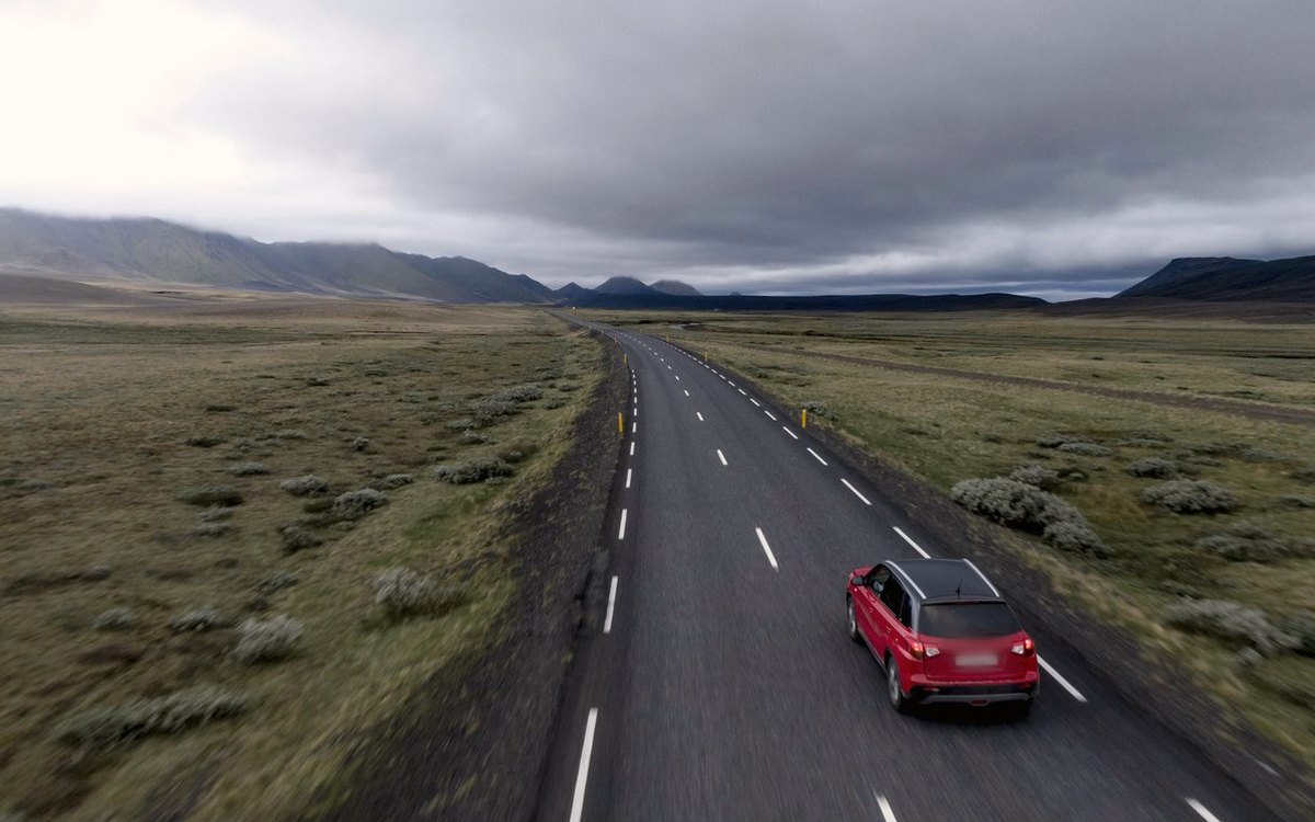 Une voiture rouge roule sur une route à travers la campagne