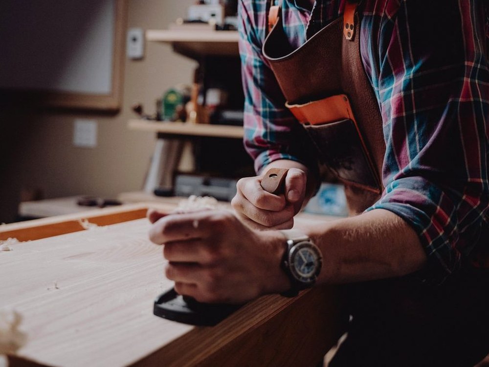 Un artisan menuisier rabote une planche dans son atelier
