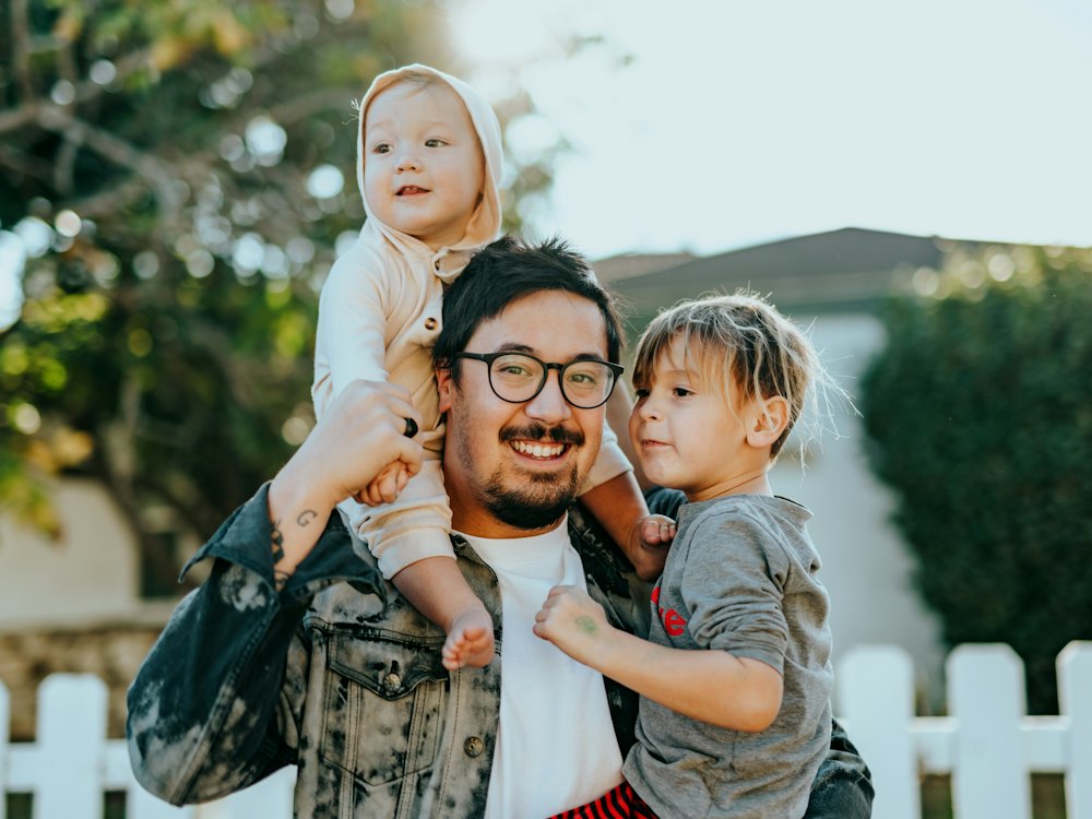 Un père porte ses deux enfants dans ses bras, en souriant